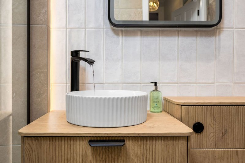 Modern bathroom with white ceramic sink, black faucet, mirror and wooden vanity