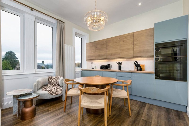 Modern kitchen-dining area with blue cabinetry, wooden dining table, chairs, and window seating