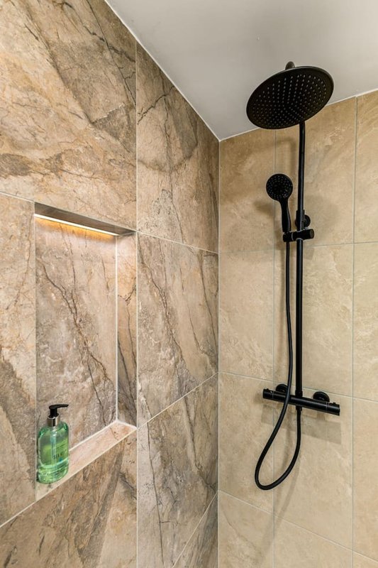 Modern bathroom shower with marble-effect tiles, black showerhead and fixtures, built-in niche