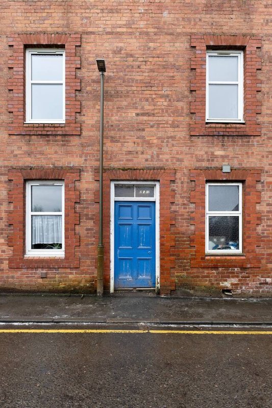 Red brick residential building facade with blue door and four sash windows