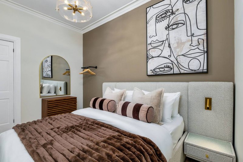 Modern bedroom with upholstered headboard, brown quilted bedding, decorative pillows and abstract wall art