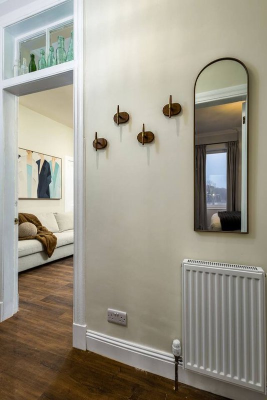 Hallway with wall sconces, mirror, radiator, and open doorway to bedroom with shelving