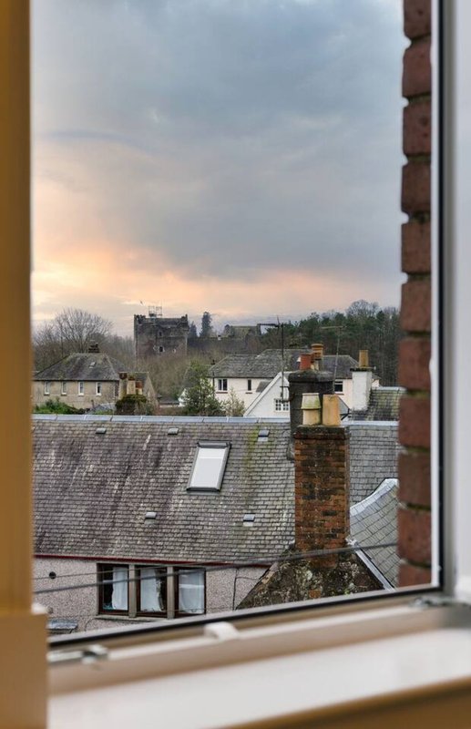 Window view of residential rooftops, chimneys, and distant countryside at dusk