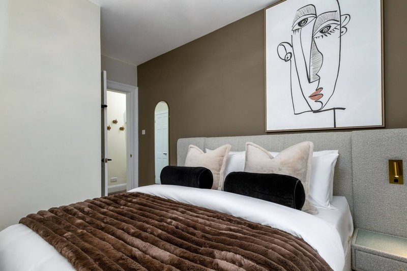 Modern bedroom with brown quilted bedding, white pillows, black cushions, and minimalist line art above bed