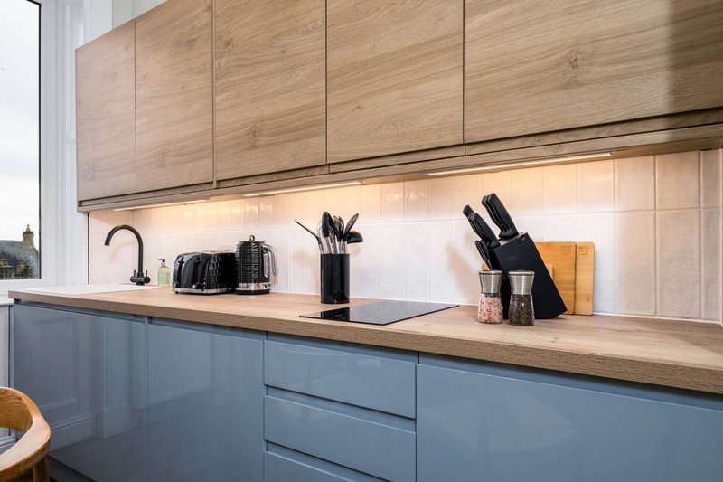 Modern kitchen with blue-grey lower cabinets, wooden countertop and upper cabinets, with utensils and appliances