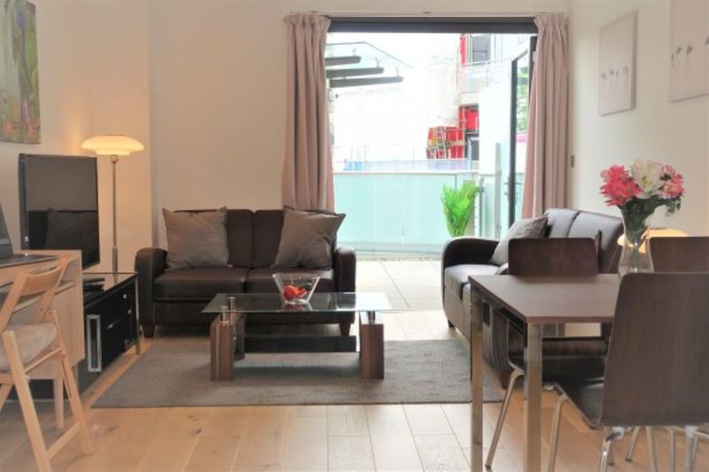 Open-plan living area with brown sofa, coffee table, dining chairs and patio doors opening to balcony