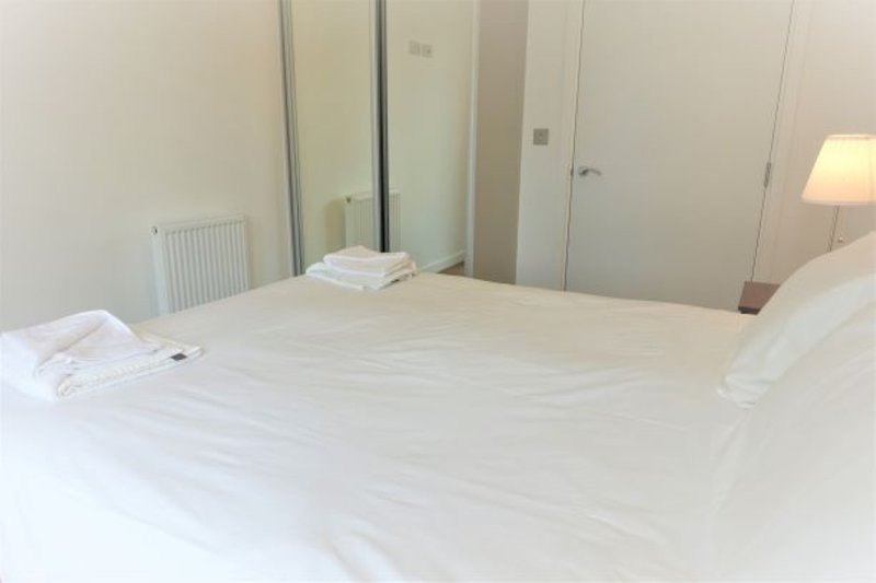 Modern bedroom with double bed, mirrored wardrobe doors, radiator and bedside lamp