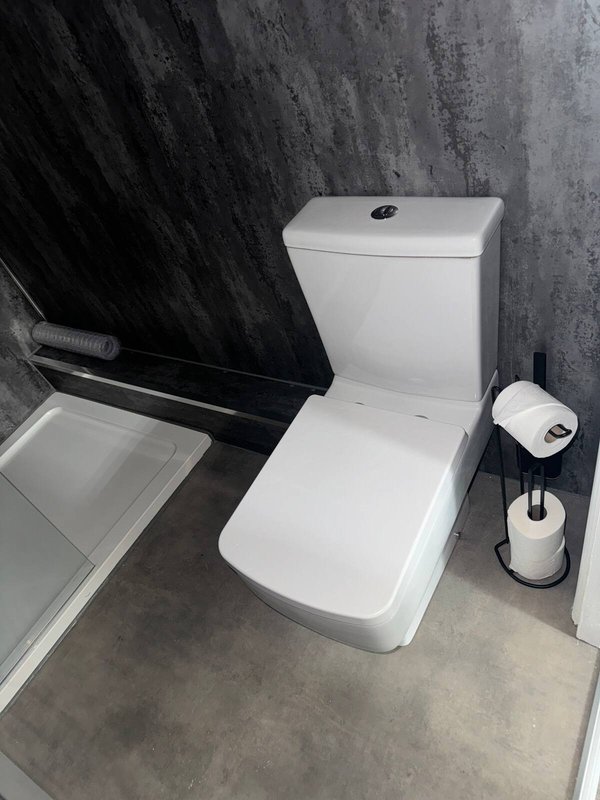Modern bathroom with white toilet, black tile walls, and paper roll holder