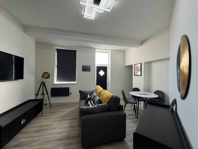 Modern living room with black sofas, wooden flooring, wall-mounted TV and decorative accents