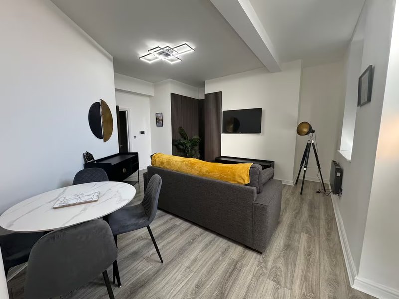 Modern open-plan living space with black sofa, yellow cushion, dining table and chairs