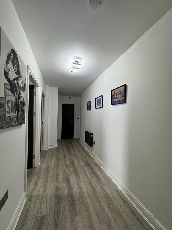 Long hallway with white walls, wooden flooring, framed artwork and closed doors