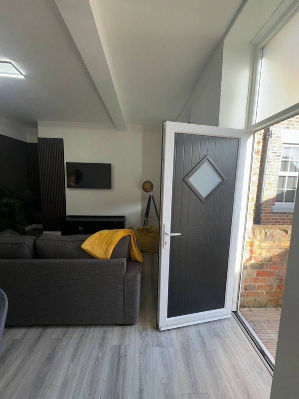 Modern living room with grey sofa, yellow throw, TV wall mount, and glass door to patio