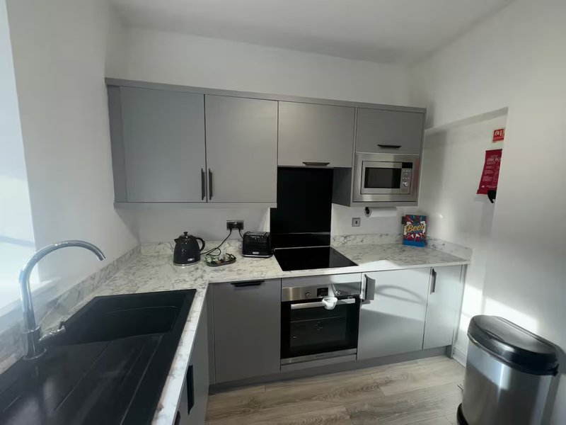 Modern kitchen with grey cabinetry, granite worktop, black stovetop and stainless steel appliances