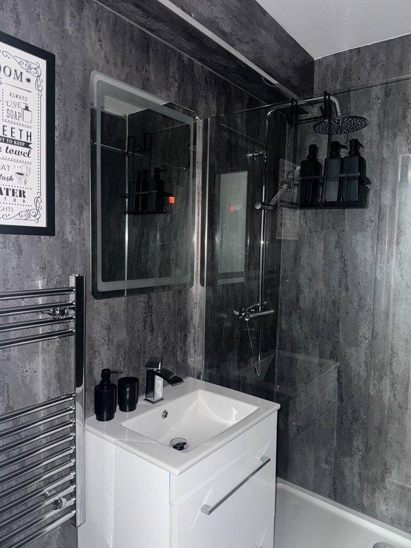 Modern bathroom with grey tile walls, white vanity sink, walk-in shower enclosure and heated towel rail