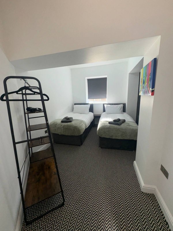 Compact bedroom with two single beds, metal shelving unit, and geometric patterned carpet