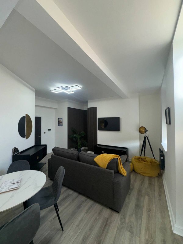 Modern studio apartment with black sofa, dining table, and kitchenette with yellow accents