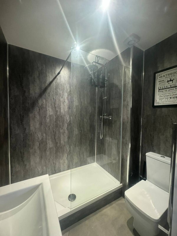 Modern bathroom with walk-in shower, white toilet, and dark tile walls