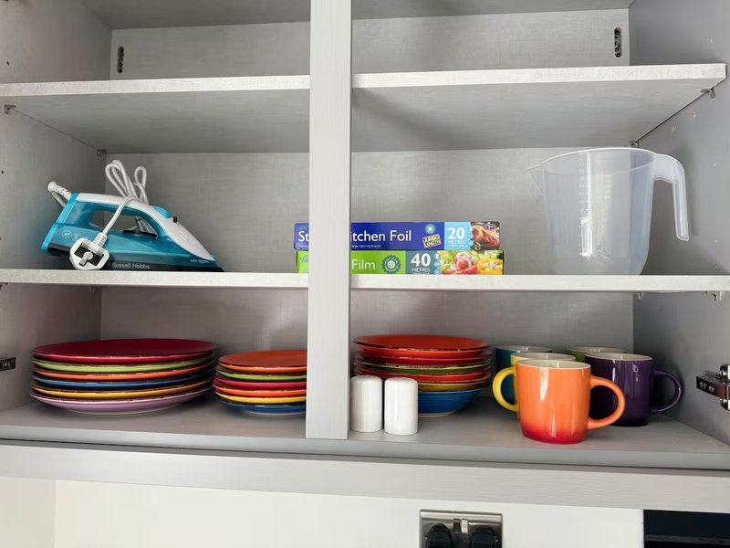 Kitchen cabinet shelves with plates, mugs, storage containers and household items
