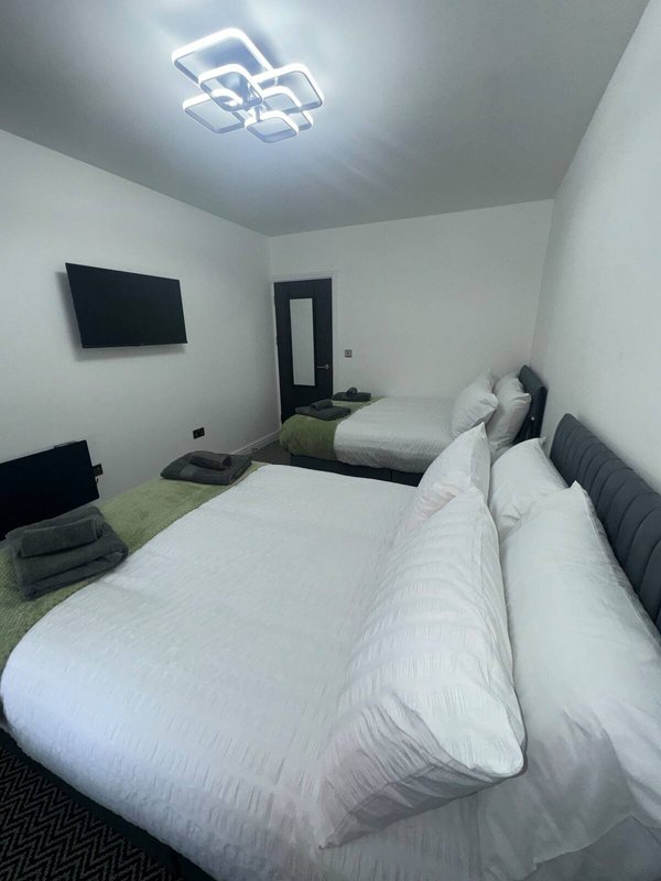 Modern bedroom with double bed, wall-mounted TV, ceiling light and dark door