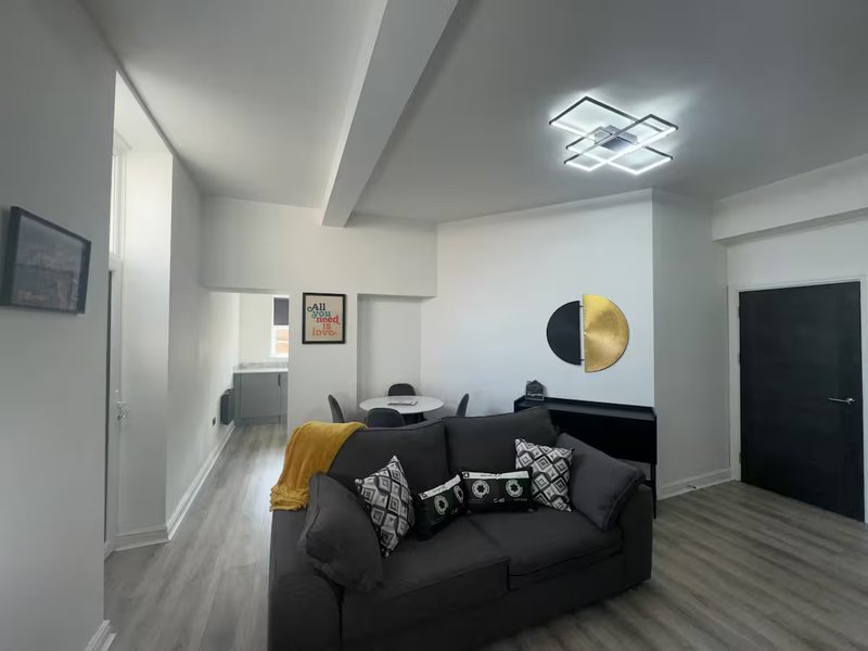 Modern living room with black sofa, yellow and white decor, geometric wall art, and wooden flooring