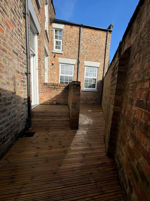 Narrow brick-walled alleyway with wooden decking and exterior stairs to residential building