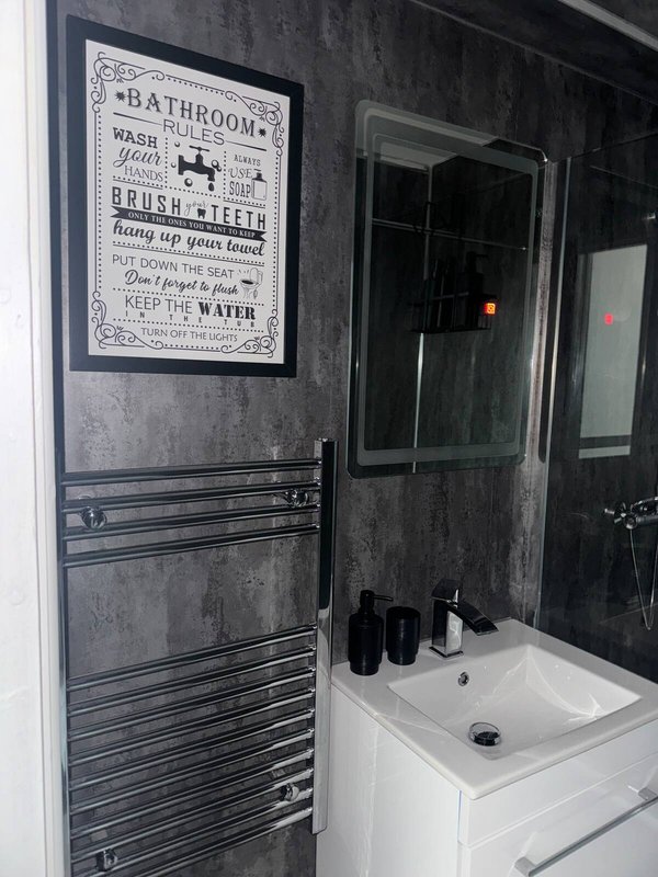 Modern bathroom with white sink, dark shower enclosure, heated towel rail and framed bathroom rules poster