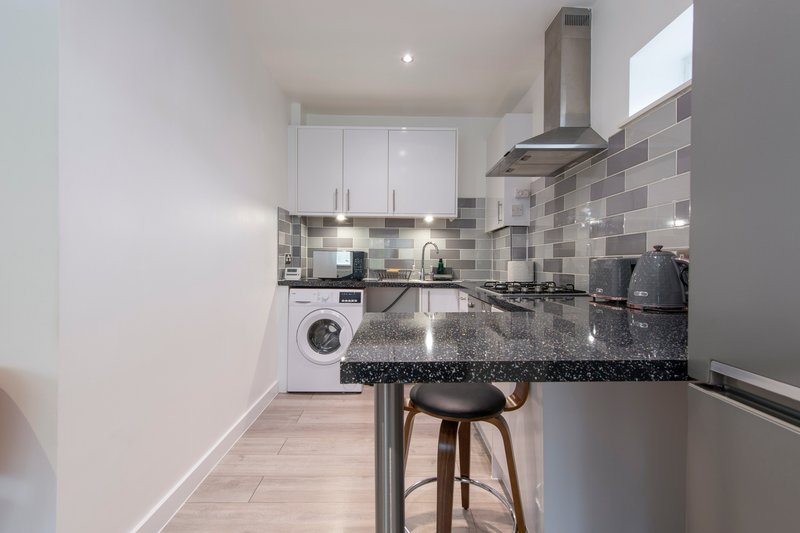 Modern kitchen with white cabinetry, grey tile backsplash, black countertop and bar seating