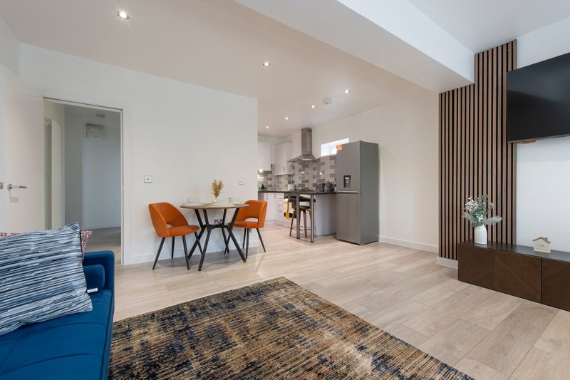 Open-plan living area with dining table, orange chairs, kitchen, and wall-mounted TV