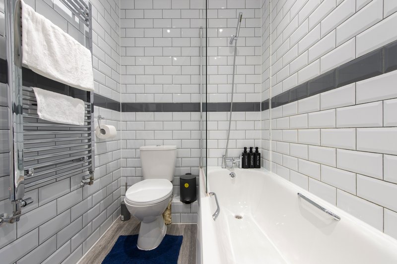 Modern bathroom with white subway tiles, toilet, bathtub, heated towel rail and navy bath mat