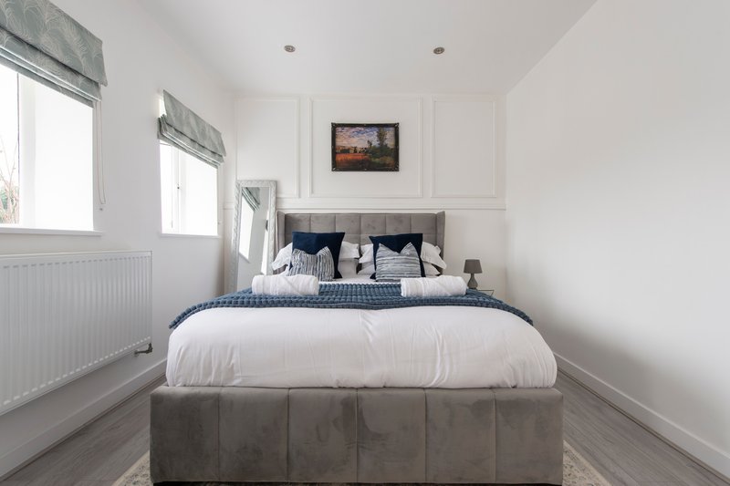 Modern bedroom with double bed, blue and white bedding, two windows, and neutral decor