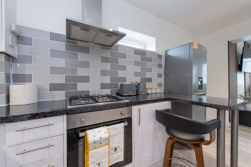 Modern kitchen with gas cooker, grey tile splashback, stainless steel appliances and bar seating