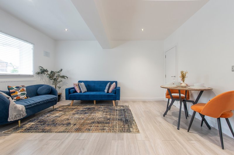 Modern living room with blue sofas, wooden dining table, orange chairs, and light wood flooring