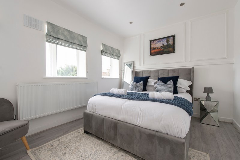 Bright modern bedroom with double bed, grey upholstered frame, white bedding and navy pillows