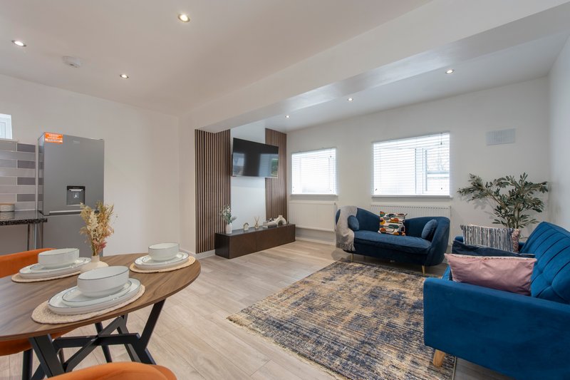 Open-plan living space with dining table, blue sofa, kitchen, and bright windows