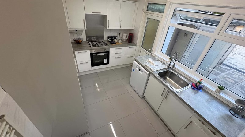 Modern kitchen with white cabinetry, gas range, sink, and large window overlooking garden