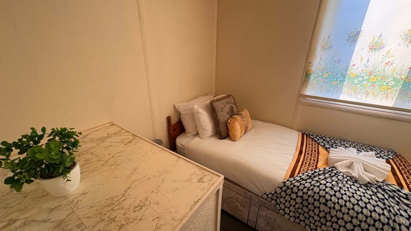 Bright bedroom with single bed, marble desk, potted plant and window with natural light