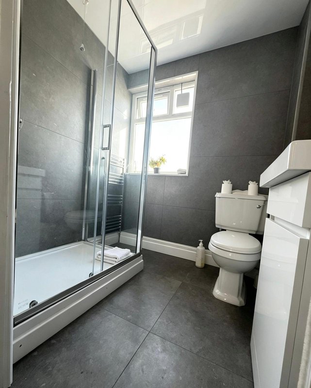 Modern bathroom with shower enclosure, toilet, sink and dark tile flooring