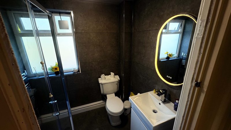 Modern bathroom with shower enclosure, toilet, vanity sink and illuminated mirror