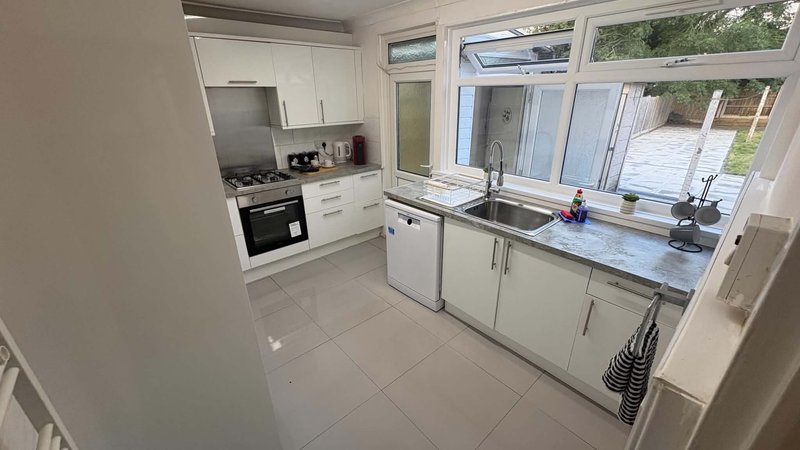Modern kitchen with white cabinetry, gas hob, sink, and garden view through large windows