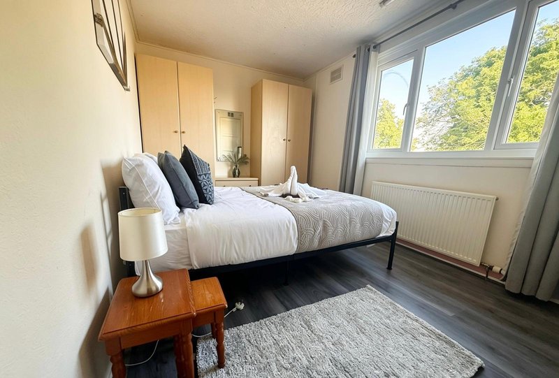 Modern bedroom with double bed, wooden nightstand, wardrobe and large windows overlooking garden