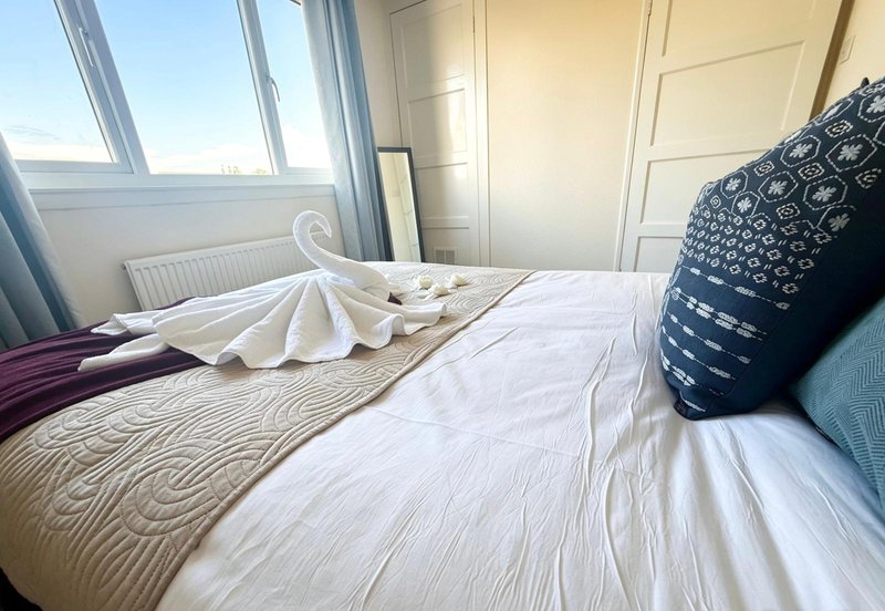Bright bedroom with double bed, patterned bedding, decorative pillows and large windows