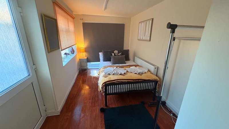 Bedroom with wooden bed frame, bedding, wooden flooring, desk area, and window with natural light
