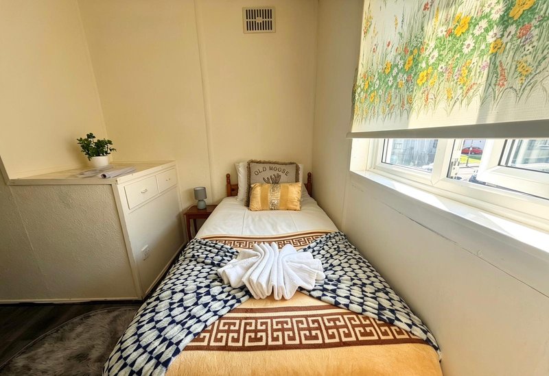 Compact bedroom with single bed, patterned rug, small desk, and window with floral blind