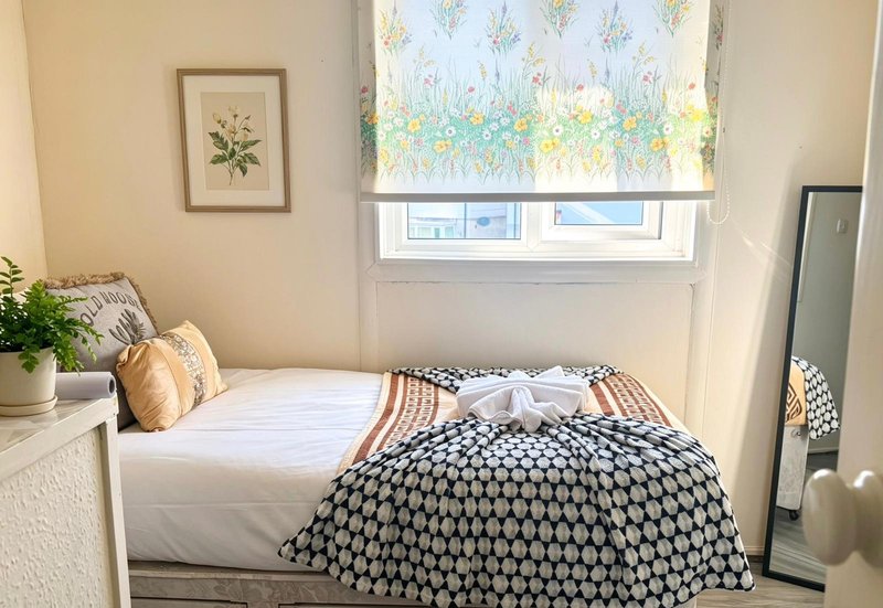 Bright bedroom with single bed, patterned bedding, cushions, and window with floral blind