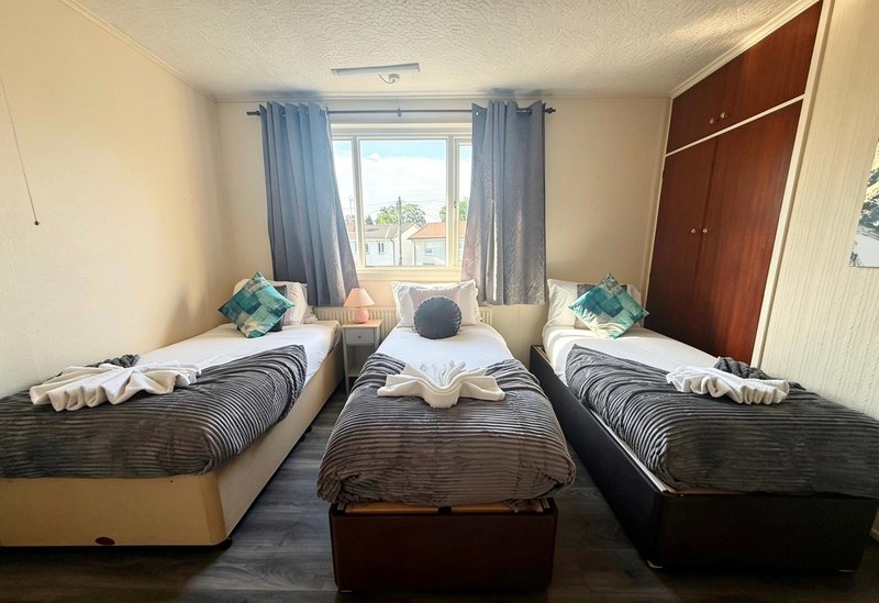 Triple bedroom with three single beds, blue curtains, wooden wardrobe, and window view