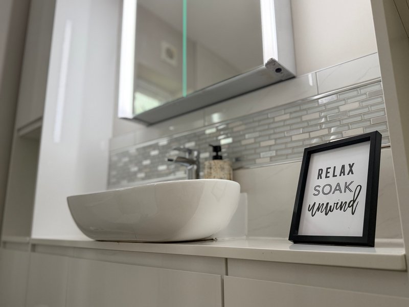 Modern bathroom with white vessel sink, illuminated mirror, tile backsplash and decorative frame