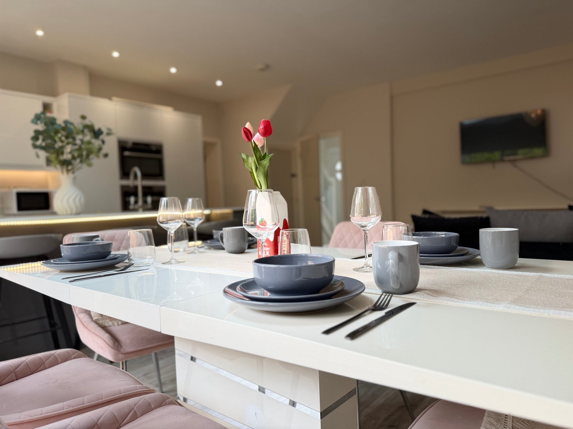 Modern open-plan kitchen and dining area with white island, place settings, and fresh flowers