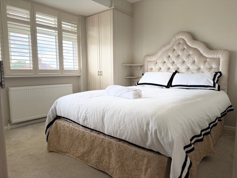 Bright bedroom with double bed, upholstered headboard, white bedding and shuttered windows