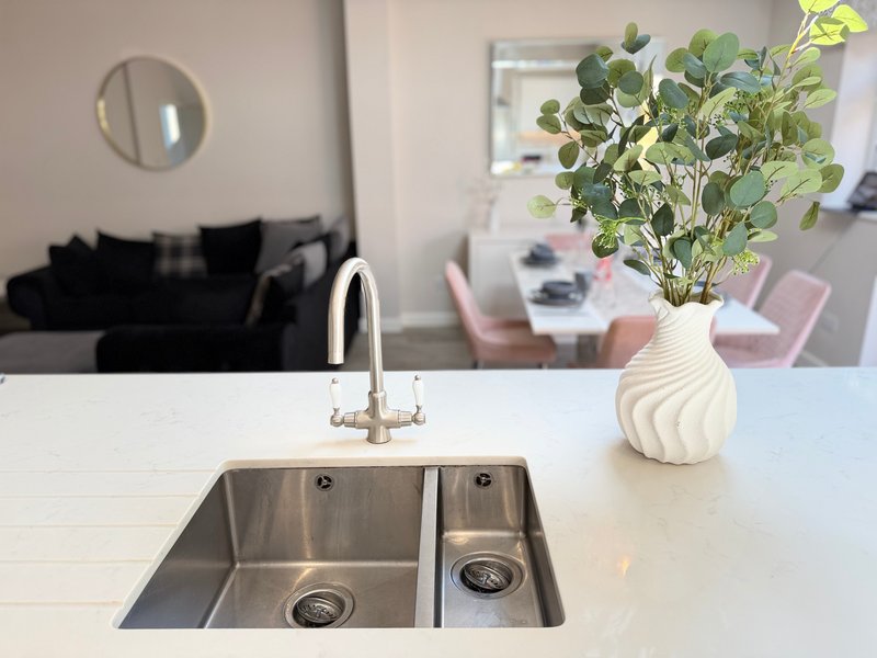 Modern kitchen island with stainless steel sink, white countertop, and potted plant in vase