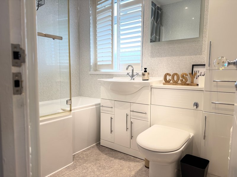 Modern bathroom with white vanity, toilet, shower enclosure and window with shutters